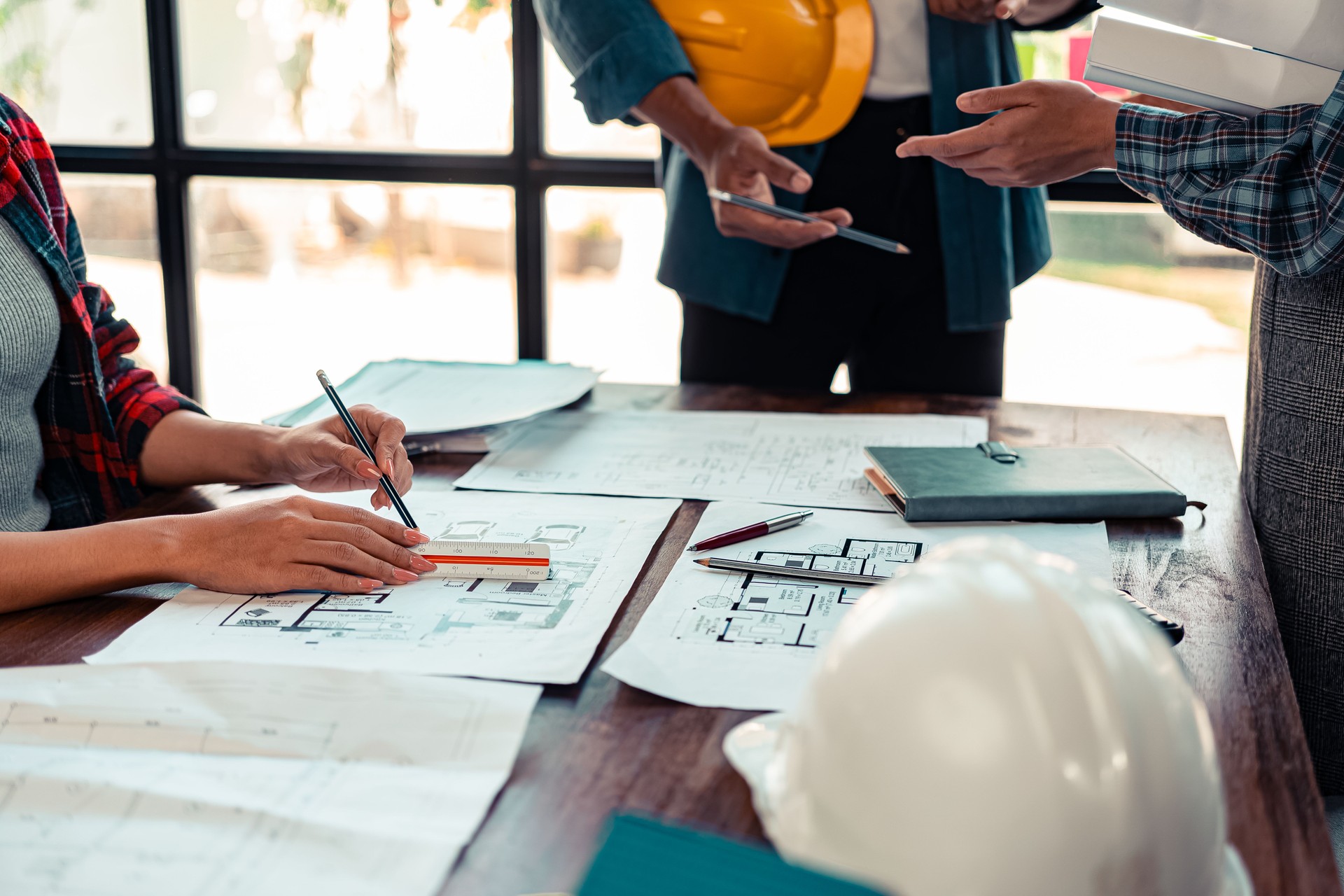 A team of industrial engineers meets to analyze machine blueprints. Discuss the project on the table, use the laptop to draw the building design project in the office. construction concept